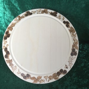 May include: A round wooden serving tray with a white background and a brown border design of blackberries and leaves.