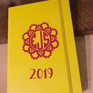 Puede incluir: Planificador amarillo con un monograma rojo y el año 2019 impreso en la portada.