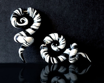 May include: A pair of black and white spiral-shaped ear gauges. The gauges are made of a smooth, shiny material and have a swirling pattern.