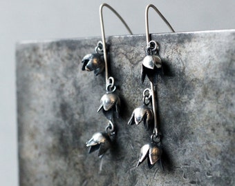 May include: Silver dangle earrings with a cluster of five bell-shaped charms hanging from each earring.