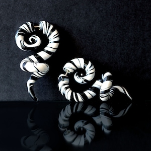 May include: A pair of black and white spiral-shaped ear gauges. The gauges are made of a smooth, shiny material and have a swirling pattern.
