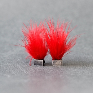 Puede incluir: Un par de pendientes con detalles de plumas de color rojo brillante. Los pendientes son de plata y tienen forma cuadrada.