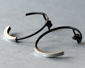 May include: A pair of hoop earrings, one with a black finish and the other with a silver finish. Both earrings have a slightly squared shape.
