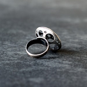May include: A silver ring with a unique, circular design featuring multiple cutouts. The ring is made of two pieces, a band and a decorative top.