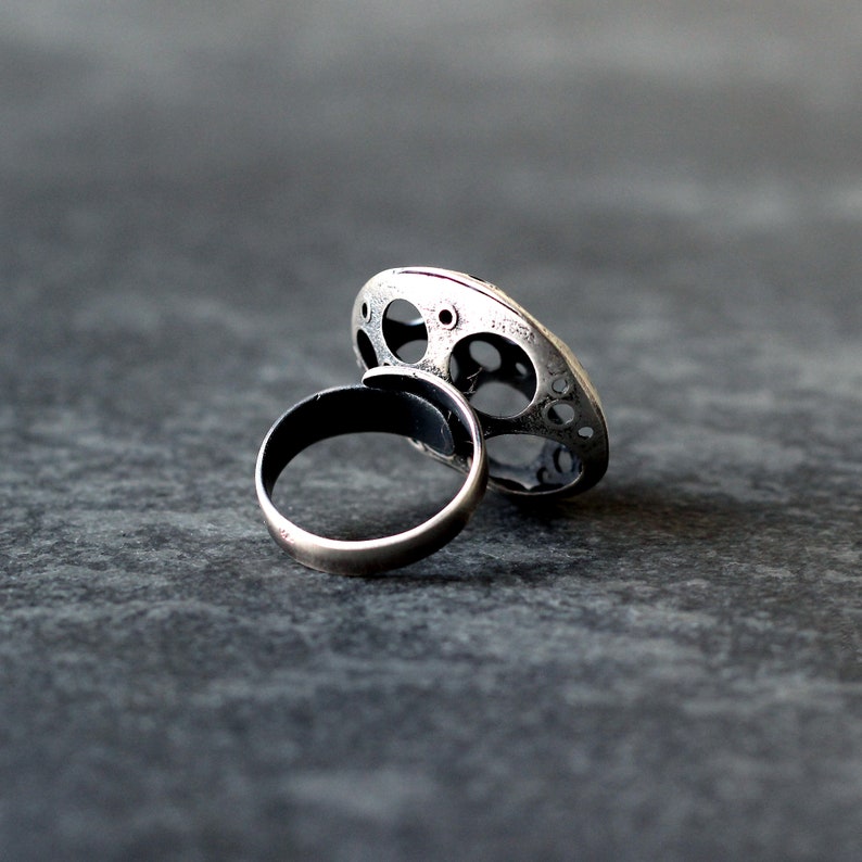 May include: A silver ring with a unique, circular design featuring multiple cutouts. The ring is made of two pieces, a band and a decorative top.