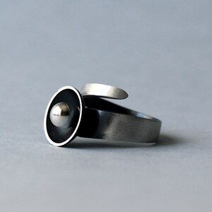 May include: A silver ring featuring a black and silver disc with a silver ball at its centre.