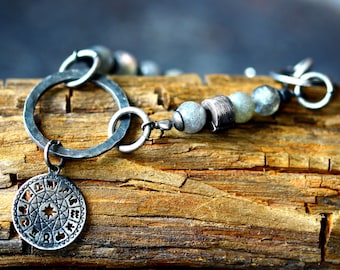 May include: A silver bracelet with a round charm featuring a zodiac wheel design. The bracelet is made with silver beads and a silver chain. The charm is attached to the chain with a silver ring.