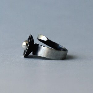 May include: A silver ring featuring a black and silver orb design. The ring is open and has a smooth, brushed finish.