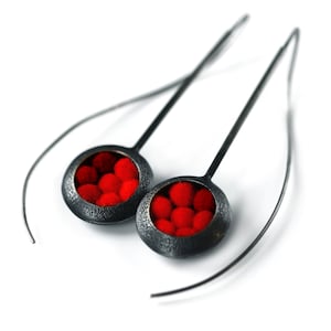 May include: A pair of silver earrings with red felt balls inside the circular pendant.