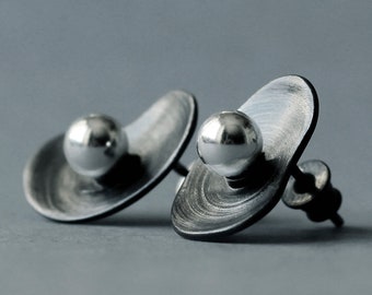 May include: A pair of silver earrings with a textured, oval-shaped base and a round silver ball on top.
