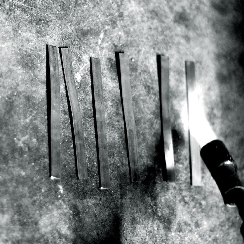 May include: A close-up of six metal strips being heated with a blowtorch. The metal strips are arranged vertically and are being heated from the bottom up. The blowtorch is in the lower right corner of the image.
