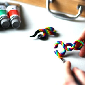 May include: Two rainbow colored spiral ear gauges. The gauges are made of polymer clay and are about 2 inches long. The gauges are on a white surface.
