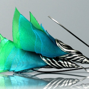 May include: A pair of silver earrings with a blue and green fabric flower design.