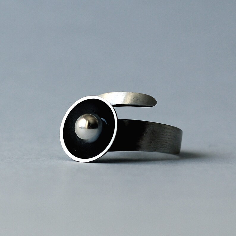May include: A silver ring featuring a black circle with a silver sphere at its centre.