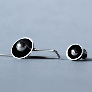 May include: A pair of silver earrings with black and silver circles. The earrings have a small silver ball in the center of the circle.