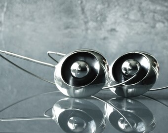 May include: A pair of silver earrings with a black center and a round shape. The earrings are suspended from thin silver wires.