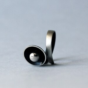 May include: A silver ring with a unique design featuring a circular, raised, and slightly domed centre piece.