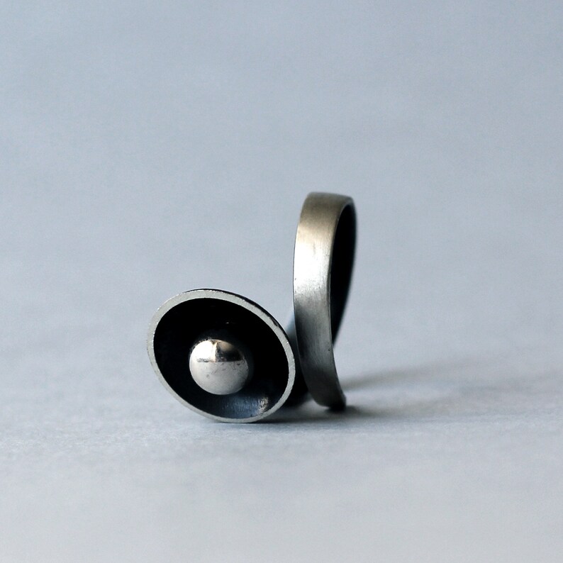 May include: A silver ring with a unique design featuring a circular, raised, and slightly domed centre piece.