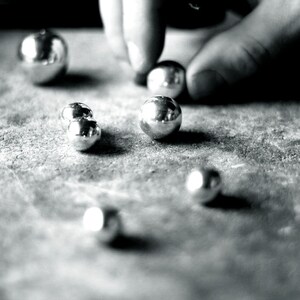 May include: A close-up of a group of silver-coloured metal balls on a textured surface. The balls are arranged in a random pattern, and some are slightly out of focus.