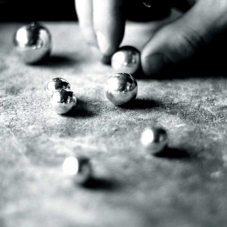 May include: A close-up of a group of silver-coloured metal balls on a textured surface. The balls are arranged in a random pattern, and some are slightly out of focus.