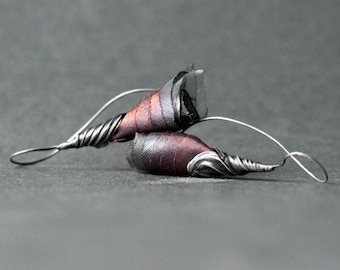 May include: A pair of silver earrings with a unique design featuring a twisted wire and a fabric flower. The flower is made of a dark red and black fabric.