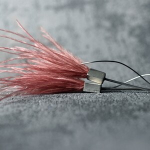 May include: A pair of earrings with a silver metal base and a cluster of pink feathers.