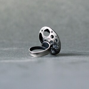 May include: A silver ring with a large, round, openwork design. The ring is made of metal and has a textured surface.