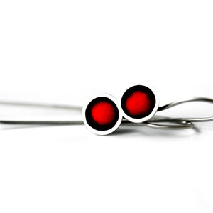 May include: A pair of silver earrings with red circular accents. The earrings have a simple, minimalist design.