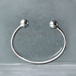 Op de afbeelding: Een zilveren armband met twee ronde, gladde, zilveren ballen aan de uiteinden.