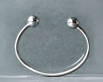 Op de afbeelding: Een zilveren armband met twee ronde, gladde, zilveren ballen aan de uiteinden.