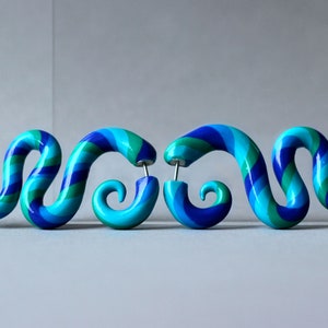 May include: A pair of blue, green, and purple spiral shaped earrings. The earrings are made of polymer clay and have a shiny finish.