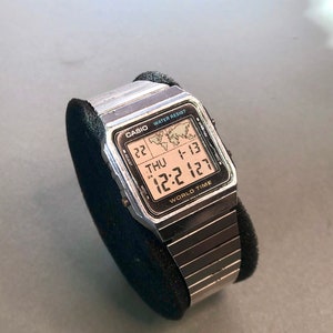 May include: A silver Casio World Time watch with a black digital display showing the time, date, and day of the week. The watch has a silver metal strap.