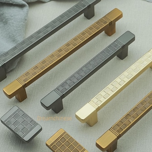 May include: A collection of cabinet hardware, including several rectangular bar pulls and matching square knobs. The pulls and knobs are in various metallic finishes, including gold, silver, and bronze. The hardware features a grid pattern design.