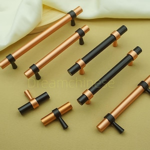 Op de afbeelding: Een verzameling meubelbeslag met een mix van stang- en knopgrepen. De grepen hebben een koperen afwerking met zwarte accenten. De stanggreeptrekken zijn lang en cilindrisch, terwijl de knoppen korter zijn. Meubelbeslag.