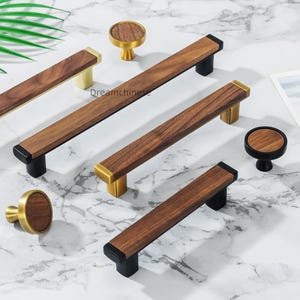 May include: A collection of wooden cabinet hardware, including pulls and knobs. The pulls have a rectangular shape with a dark wood grain center and brass or black accents. The knobs are round with a wood grain top and brass or black base.