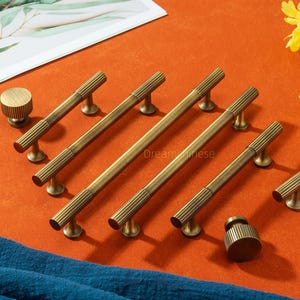 Op de afbeelding: Een verzameling antieke messing kastbeslagen, waaronder handgrepen en knoppen. De handgrepen hebben een geribbeld ontwerp en zijn er in verschillende maten. De knoppen zijn rond met een bijpassende geribbelde textuur.