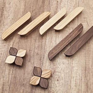 Peut inclure: Un ensemble de boutons de cabinet en bois dans deux styles. Le premier style est une forme rectangulaire arrondie simple en bois clair. Le deuxième style est une forme de fleur à quatre feuilles avec une alternance de bois clair et foncé.