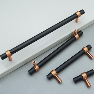 May include: Five black cabinet pulls with copper accents. The pulls are in various sizes and shapes, including a long bar pull, a shorter bar pull, and two small T-shaped pulls.