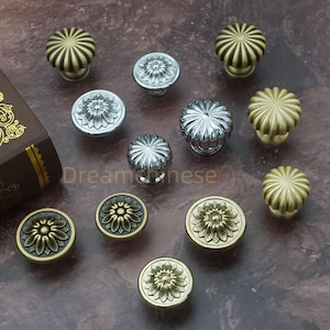 Può includere: Una collezione di pomelli decorativi per mobili in varie finiture metalliche, tra cui argento e oro. I pomelli presentano disegni floreali e scanalati. L'immagine include il testo "Dreamchinese".