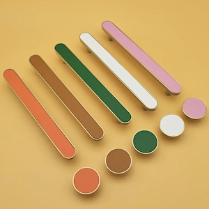 May include: Assortment of colorful cabinet knobs and pulls in various colors, including pink, white, green, brown, and orange. The knobs and pulls are made of metal and have a polished finish.