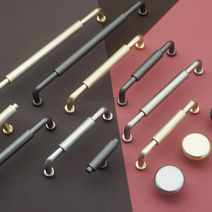 May include: A collection of cabinet hardware, including bar pulls and knobs, in various metallic finishes. The pulls have a straight center section and curved ends. Finishes include gold, black, and silver. The knobs are round and have a matching finish.