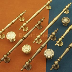 May include: An assortment of antique brass cabinet hardware, including knobs and pulls. The hardware features ornate designs with a warm, golden finish. The image shows various sizes and styles of the hardware, suitable for drawers and cabinets.