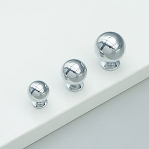 Op de afbeelding: Drie zilveren ronde kastknoppen in verschillende maten. De knoppen zijn glanzend en hebben een glad oppervlak.