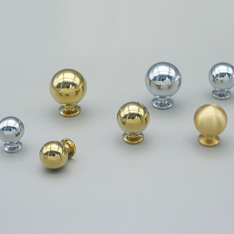 Op de afbeelding: Assortiment van zes ronde kastknoppen in gouden en zilveren afwerkingen. De knoppen hebben een glad, glanzend oppervlak en zijn ontworpen voor gebruik op lades en deuren.