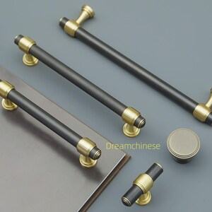 May include: A selection of cabinet hardware, including black and gold-toned handles and a knob. The handles have a black cylindrical centre with gold detailing and mounting bases. The knob is round with a gold finish. Suitable for furniture.