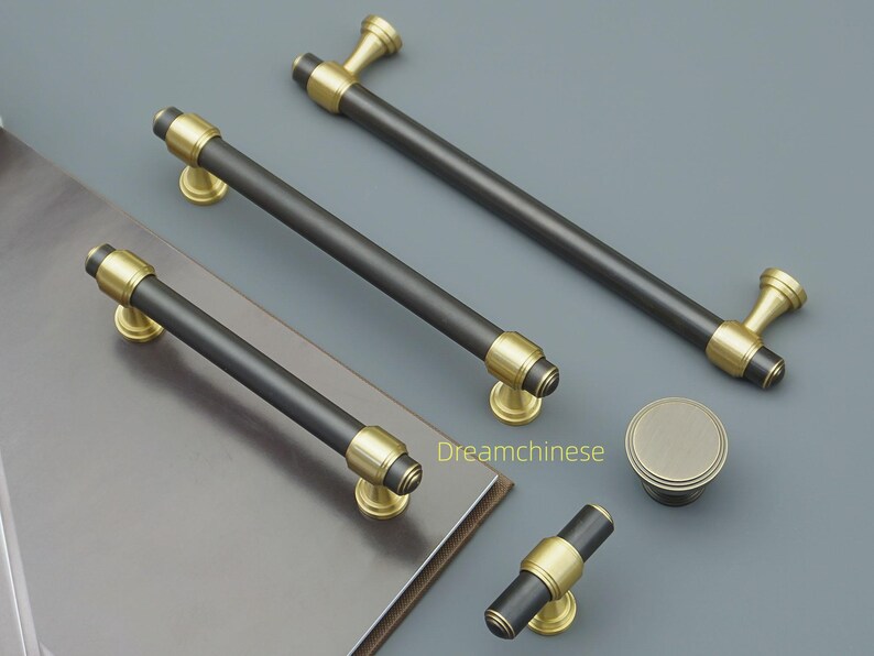 May include: A selection of cabinet hardware, including black and gold-toned handles and a knob. The handles have a black cylindrical centre with gold detailing and mounting bases. The knob is round with a gold finish. Suitable for furniture.