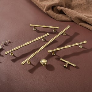 Op de afbeelding: Een verzameling antieke messing kastbeslagen, waaronder handgrepen in verschillende maten en een ronde knop. De hardware heeft een bamboe-ge&iuml;nspireerd ontwerp, met een warme, gouden tint. De stukken zijn gerangschikt op een bruin oppervlak.