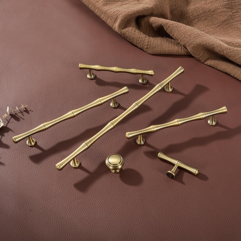 Op de afbeelding: Een verzameling antieke messing kastbeslagen, waaronder handgrepen in verschillende maten en een ronde knop. De hardware heeft een bamboe-ge&iuml;nspireerd ontwerp, met een warme, gouden tint. De stukken zijn gerangschikt op een bruin oppervlak.