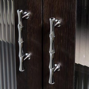 Op de afbeelding: Close-up van twee kastdeuren met gepolijste zilveren handgrepen in de vorm van bamboe. De deuren zijn van donkerbruin hout met een zichtbare nerf. De handgrepen zijn gemonteerd op ronde zilveren achterplaten.