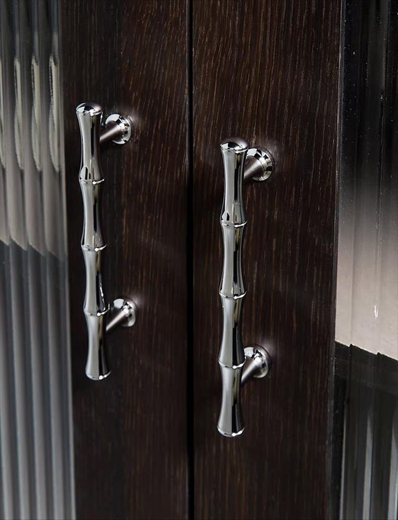 Op de afbeelding: Close-up van twee kastdeuren met gepolijste zilveren handgrepen in de vorm van bamboe. De deuren zijn van donkerbruin hout met een zichtbare nerf. De handgrepen zijn gemonteerd op ronde zilveren achterplaten.